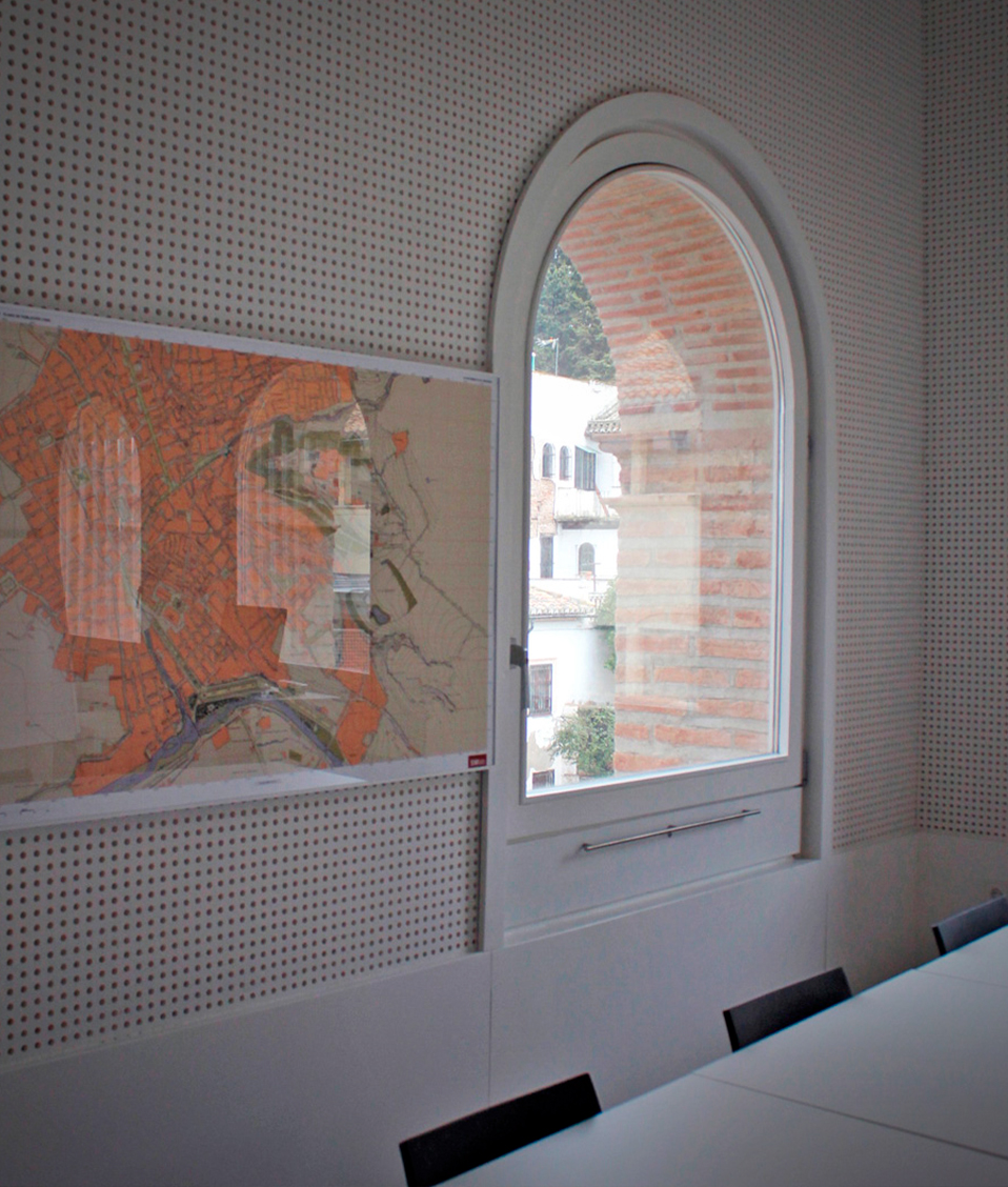 Imagen en la que se muestra un mapa de Granada enmarcado y colgado de una pared al lado de una ventana